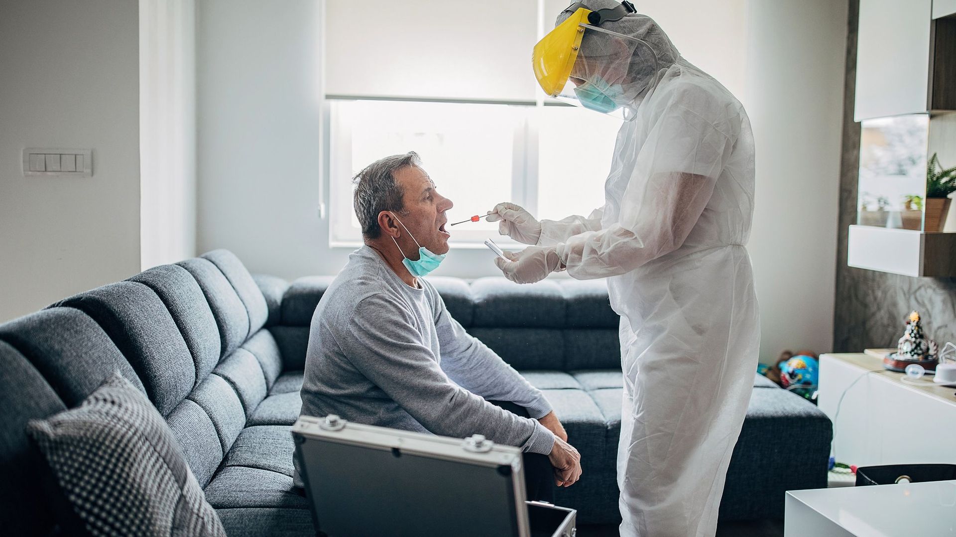 Une femme médecin effectue un prélèvement de gorge chez un homme âgé à domicile pour le test COVID-19.