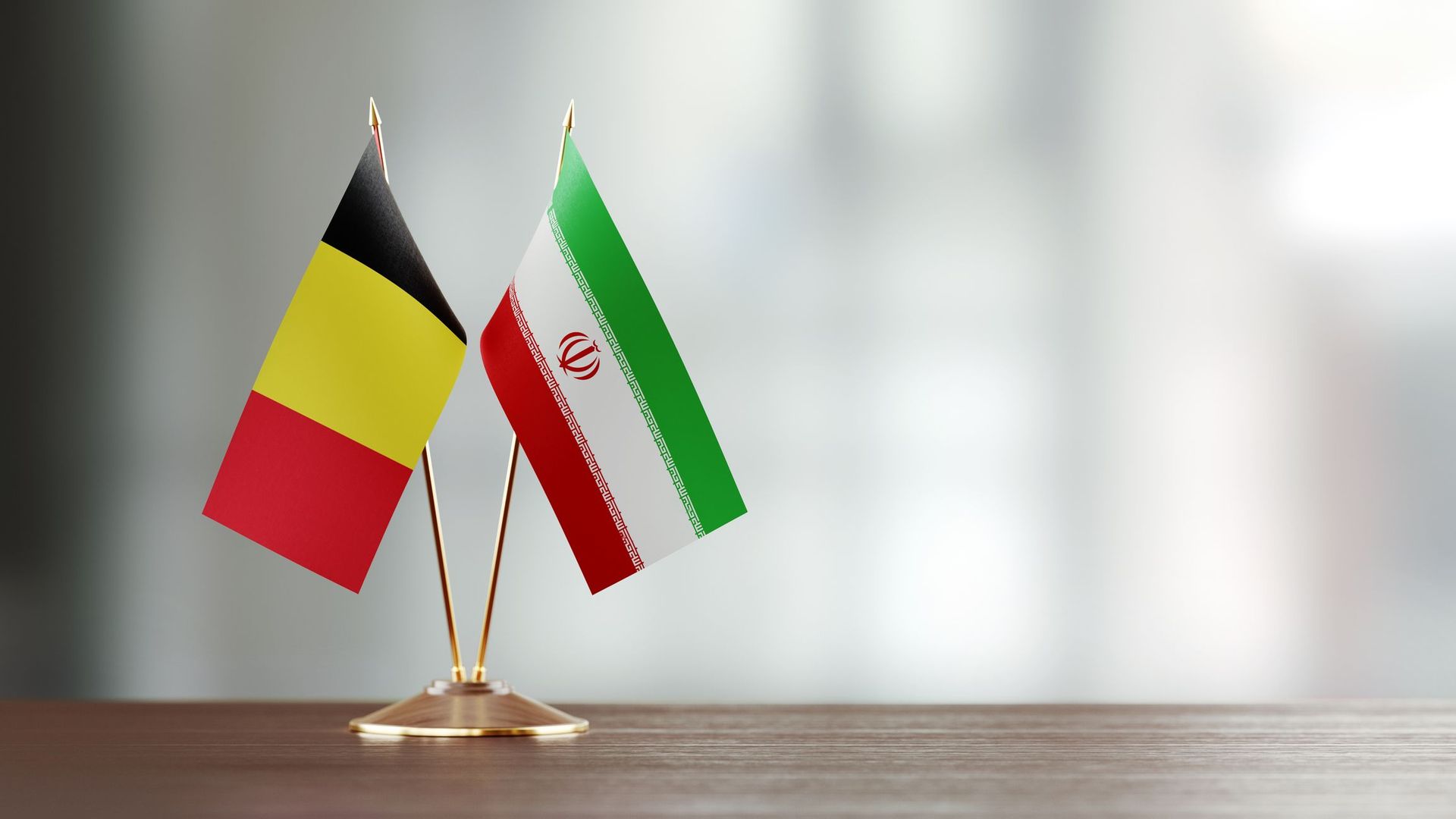 Belgian And Iranian Flag Pair On A Desk Over Defocused Background